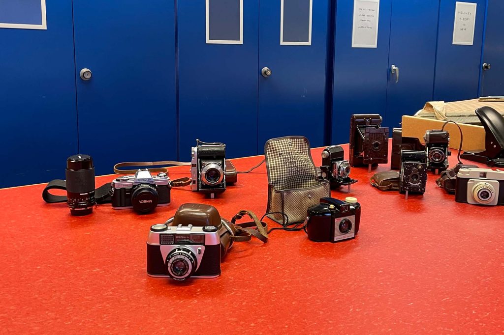 A colour picture of a selection of cameras lying on an orange bench.